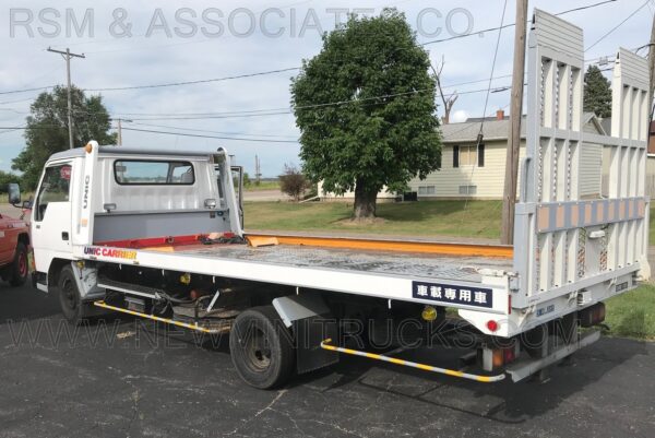 A flatbed truck parked in the street next to a tree.